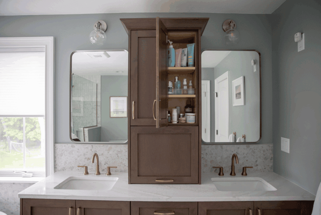 Open center vanity storage tower with organized shelving between dual sinks in WoodHarbor cherry Cashmere cabinetry with champagne bronze hardware showing bathroom organization solution