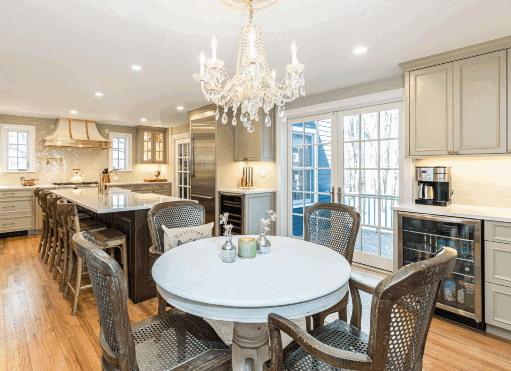 Belle Maison French-inspired luxury kitchen renovation featuring distressed walnut island, gray cabinetry, crystal chandelier, and round dining table