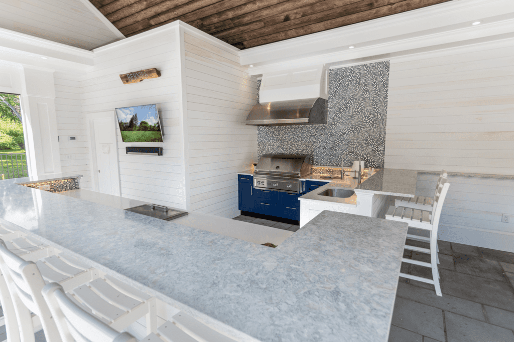 Outdoor kitchen with white cabinetry, light gray stone counters, and a bright coastal inspired design. 