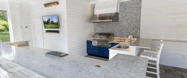 Outdoor kitchen with white cabinetry, light gray stone counters, and a bright coastal inspired design. 