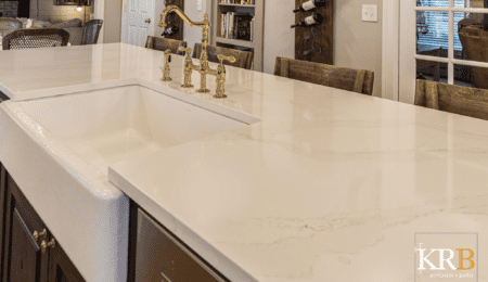 Close up of white marble countertops with farmhouse white sink and gold faucet