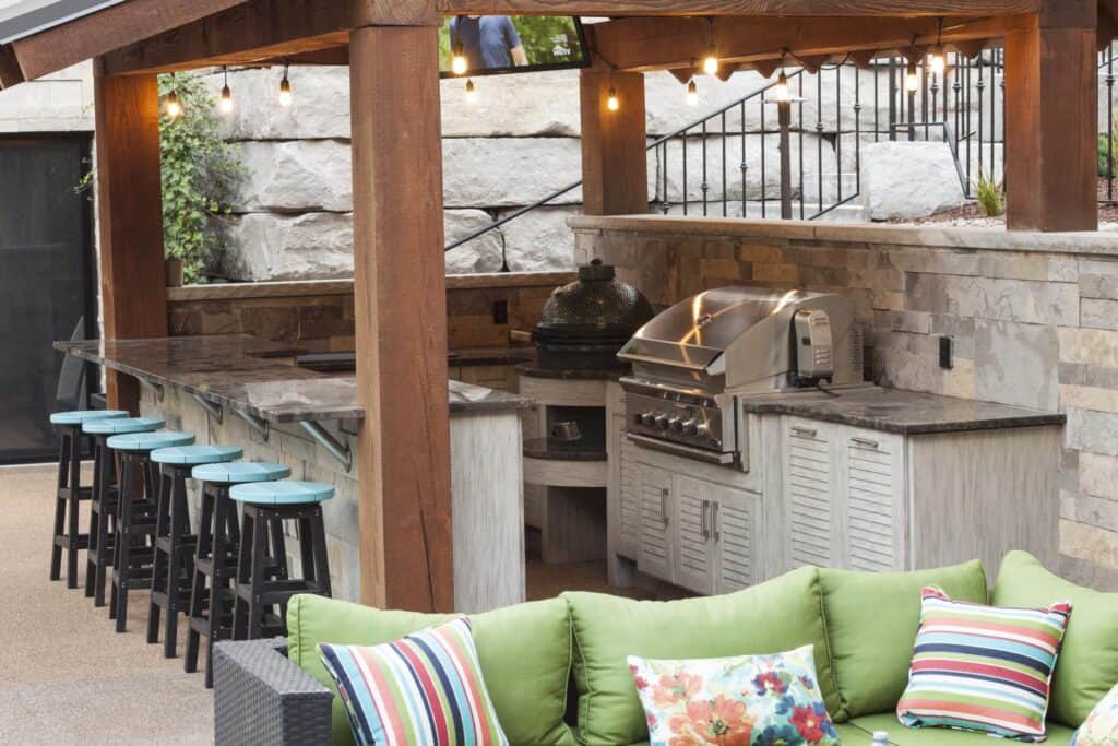 An outdoor kitchen under a pergola with bar seating. 