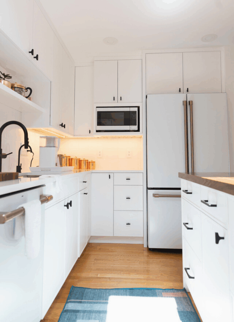 White kitchen with built-in microwave, under-cabinet LED lighting, copper canister display, and organized drawer storage in Scandinavian minimalist design