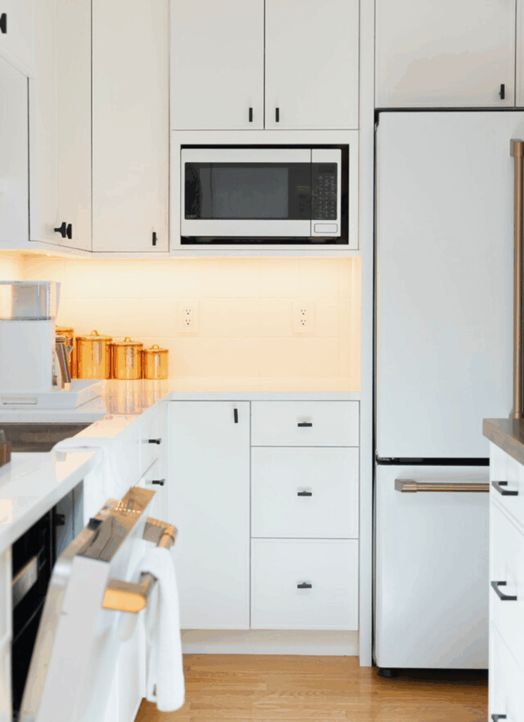 Built-in microwave wall with white shaker cabinetry, copper canister set on illuminated shelf, and under-cabinet LED task lighting in minimalist Portsmouth kitchen