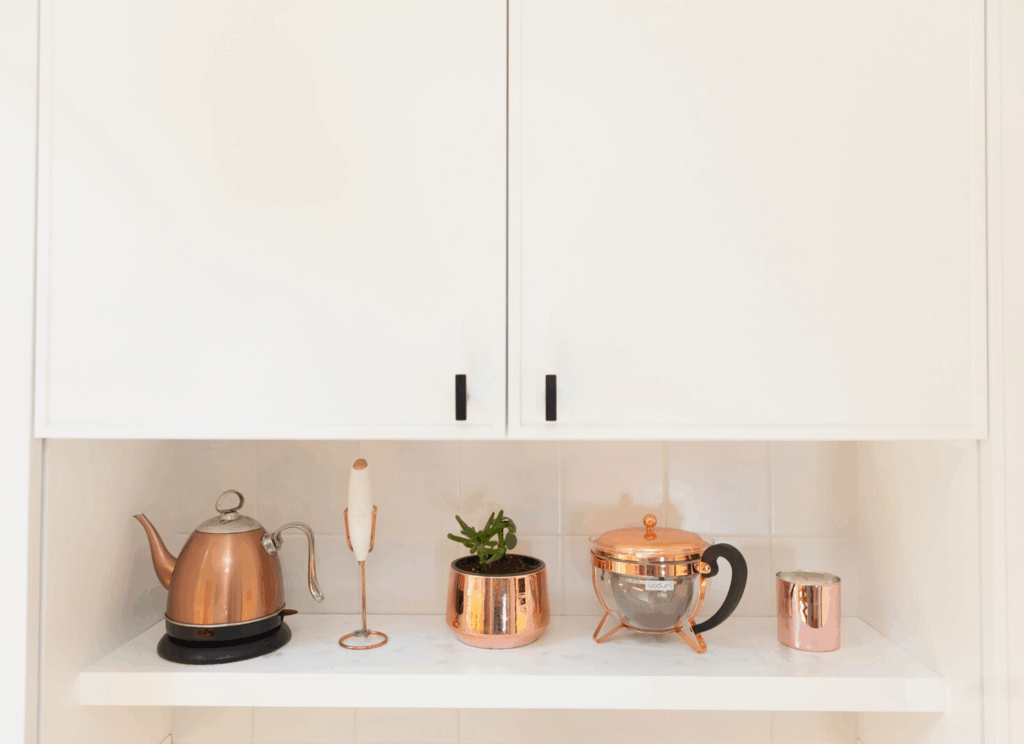Open kitchen shelving displaying copper kettle, succulent plant in copper planter, and artisan tea accessories with white subway tile backsplash in Nordic-inspired design