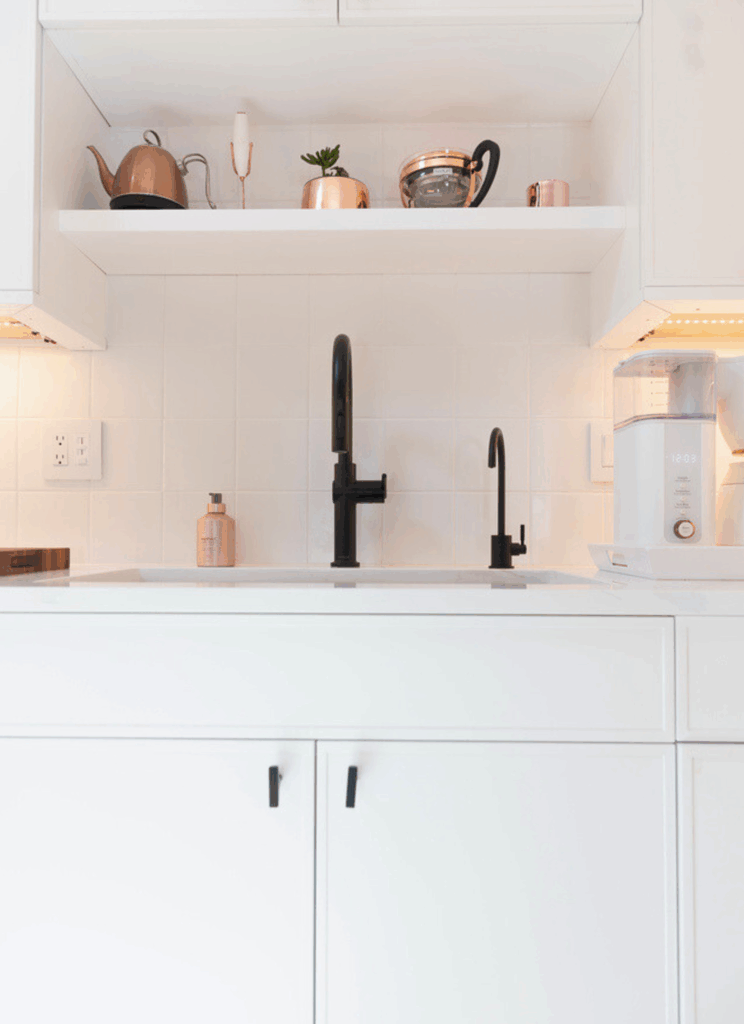 Matte black kitchen faucet and soap dispenser on white countertop with white subway tile backsplash and copper accent pieces in Scandinavian kitchen by KRB