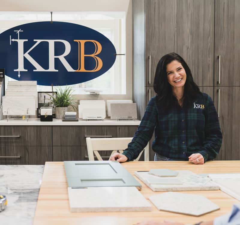 Friendly interior designer standing at table top with cabinet door samples and KRB sign in the background